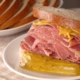 A corned beef sandwich with mustard and pickle on rye bread