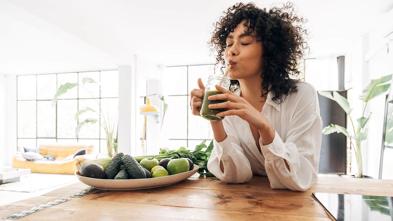 Young african american woman drinking green juice with reusable bamboo straw in loft apartment