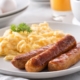 a plate of scrambled eggs and sausage with coffee and orange juice