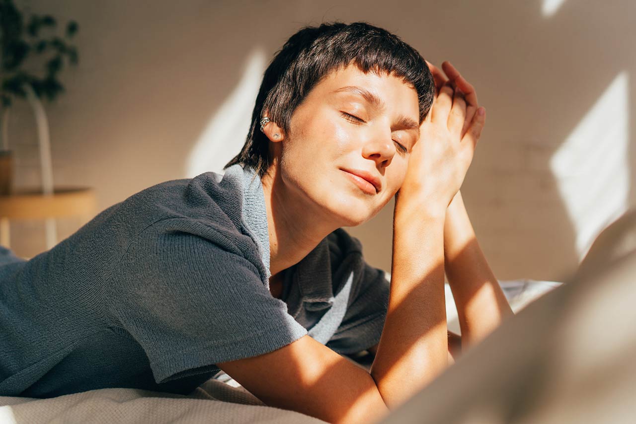 A woman lies on a bed in bright sunlight from the window