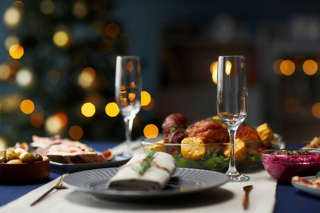 still life shot of empty champagne glass served on dining table with festive turkey dinner and colorful christmas lights in blurred background