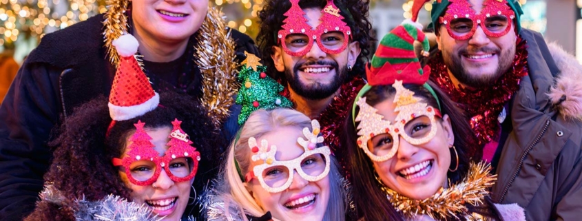 happy friends wearing glasses and santa claus hat having new year party outside under Christmas tree decoration