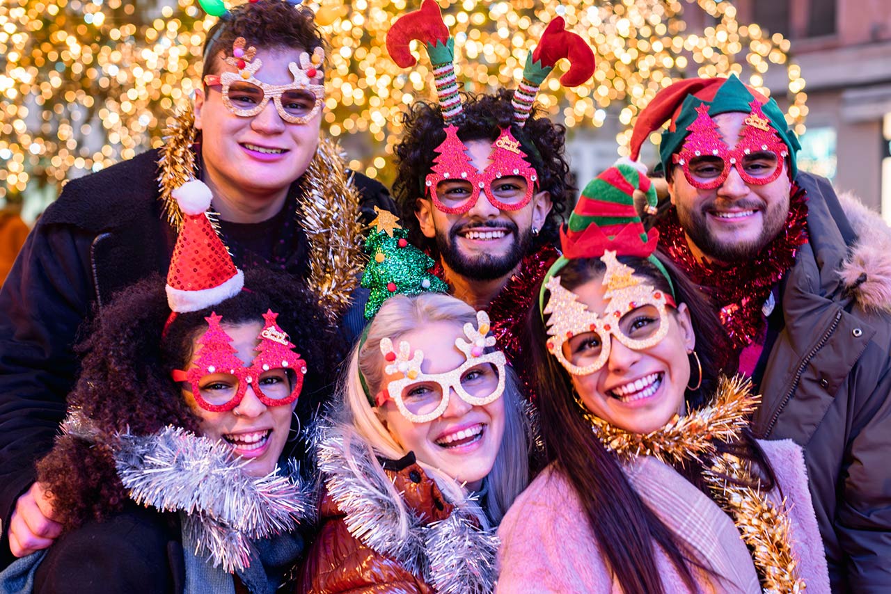 happy friends wearing glasses and santa claus hat having new year party outside under Christmas tree decoration